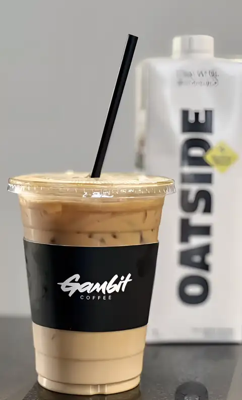 An iced latte in a clear Gambit cup next to a carton of oat milk